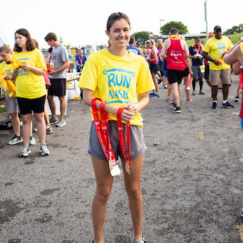 Woman wearing RunNash shirt and holding medals